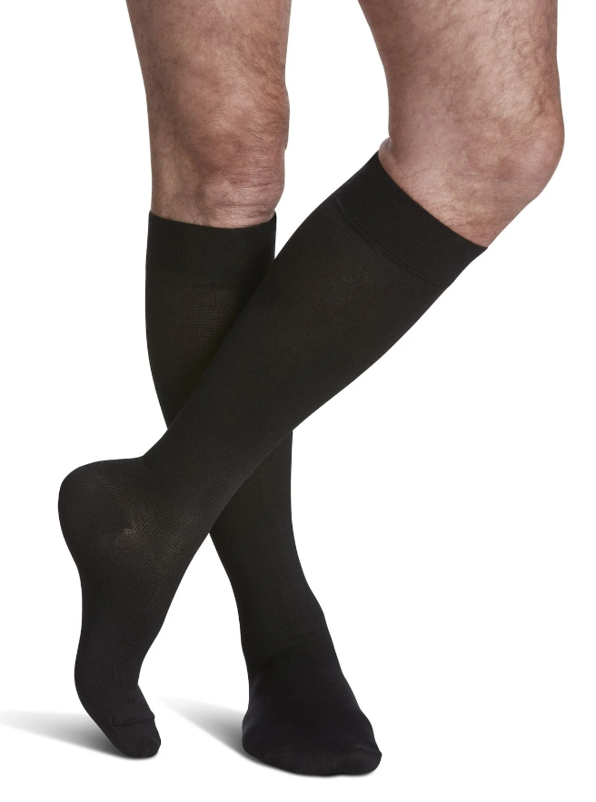 Model wearing classic black opaque Sigvaris knee-high compression socks, representing the firm-to-extra-firm 30-40 mmHg support collection.